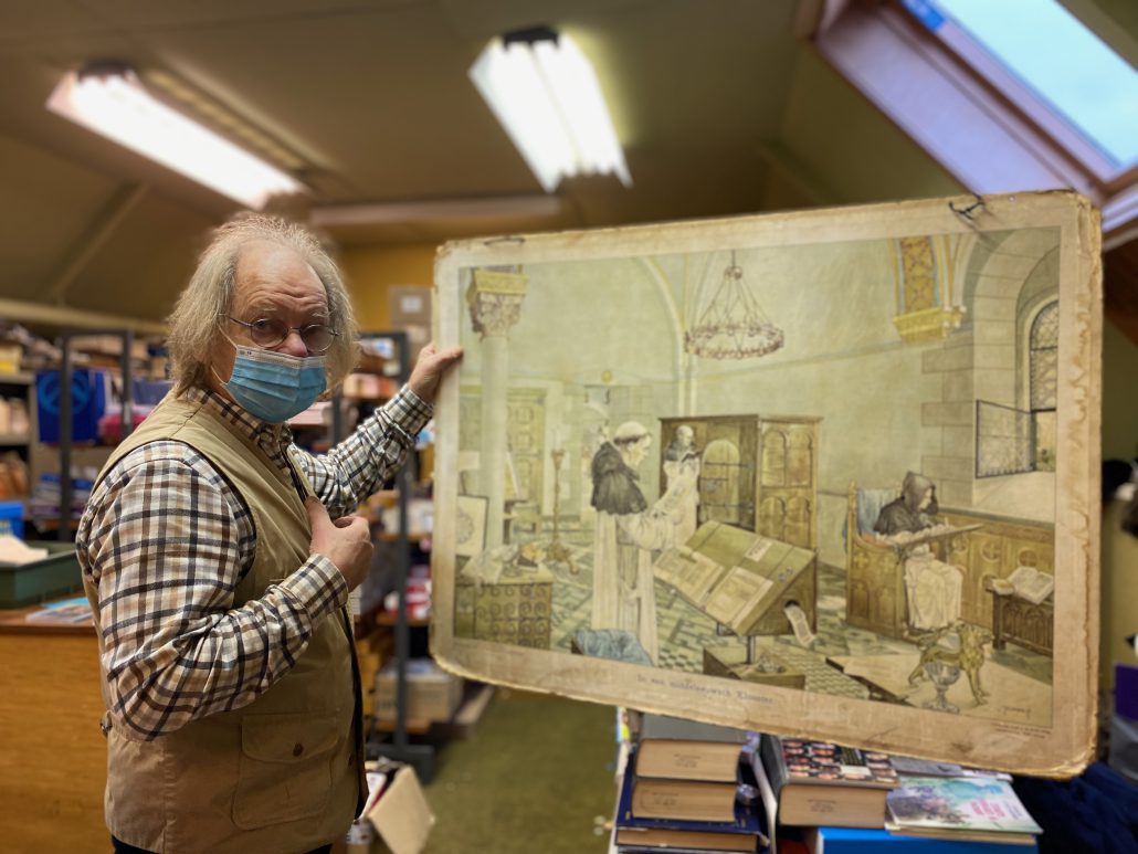 Een man laat een afbeelding zien monniken in een klooster. Het is een historische schoolkaart.